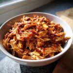 Bowl of shredded crockpot chicken recipes, coated in a rich, dark sauce, ready to serve.