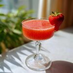 A vibrant strawberry daiquiri recipe in a stemmed glass, garnished with a fresh strawberry.