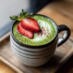 A vibrant strawberry matcha latte in a mug, garnished with fresh strawberry slices and a sprinkle of red powder.