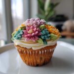Close-up of a single wildflower cupcake decorated with buttercream flowers in pink, orange, and teal.
