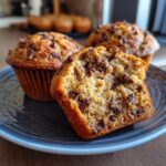 Three chocolate chip muffins greek yogurt on a plate, one muffin is cut in half to show the inside texture.