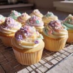 Several cute spring cupcake designs, decorated with pastel frosting and floral sprinkles on a cooling rack.