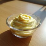 Creamy homemade mayonnaise recipe avocado oil in a clear glass bowl on a wooden surface.