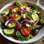 A vibrant salad with lemon vinaigrette, featuring cucumbers, tomatoes, red onion, olives, and feta cheese.