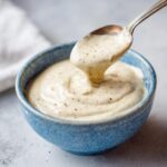 A spoonful of 5-Minute Creamy Horseradish Sauce being lifted from a blue bowl, showing its creamy texture.