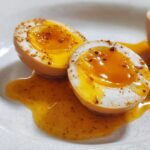 Close-up of halved addictive marinated eggs with a runny yolk and seasoning, sitting in marinade.