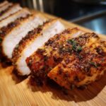 Sliced Air Fryer Chicken Breast on a wooden board, seasoned with herbs and spices. Perfectly cooked and juicy.