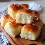 A stack of freshly baked Amazing 1-Hour Soft Dinner Rolls on a wooden board, showing their soft texture.