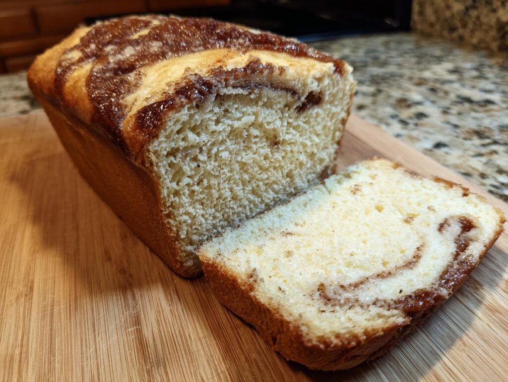 A loaf of freshly baked Amish Cinnamon Bread with a slice cut, showcasing the cinnamon swirl.