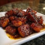 Close-up of glazed Bang Bang Salmon Bites on a white plate, ready to eat.