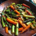 Close up of a Broccoli Mushroom Stir Fry with asparagus, carrots and onions in a copper pan.