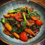 A vibrant Broccoli Mushroom Stir Fry featuring carrots, tomatoes, and sesame seeds in a blue bowl.