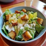 A bowl of Caesar Salad featuring romaine lettuce, creamy dressing, and golden croutons.