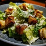 A Caesar Salad in a bowl, featuring romaine lettuce, croutons, Parmesan cheese, and dressing.