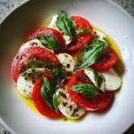 Close-up of Caprese Salad Tomato Mozzarella Basil with olive oil and herbs in a white bowl.