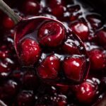 Close-up of a spoonful of thick and juicy homemade cherry pie filling, showcasing its rich color and texture.