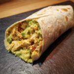A tasty Chicken Avocado Wrap with visible chicken, avocado, and tortilla on a dark surface.
