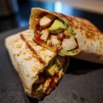 A halved Chicken Avocado Wrap showing the filling of chicken, avocado, and tomatoes.