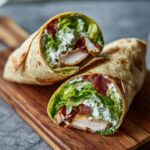 A halved Chicken Caesar Wrap on a wooden board, showcasing the chicken, lettuce, bacon, and creamy Caesar dressing.