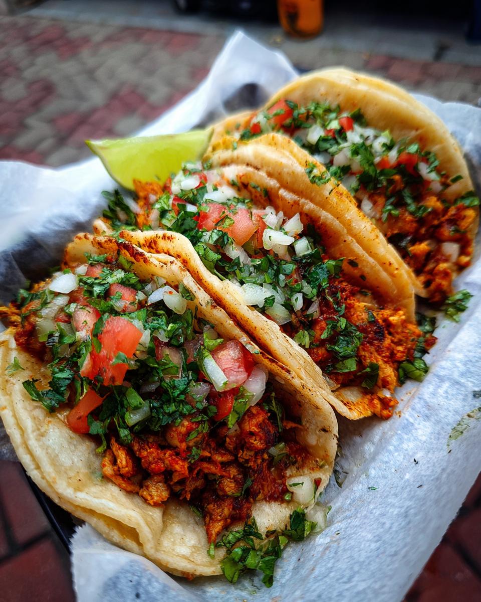 Three chicken street tacos filled with chicken, cilantro, and onions, served with a lime wedge.
