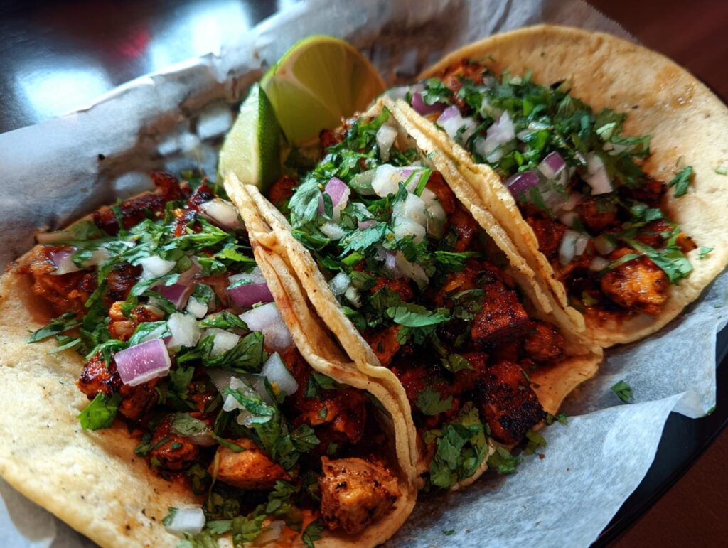 Three flavorful Chicken Street Tacos topped with cilantro, onion, and a lime wedge.