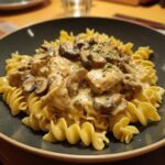 A plate of Chicken Stroganoff featuring creamy sauce, mushrooms, and chicken over spiral pasta.
