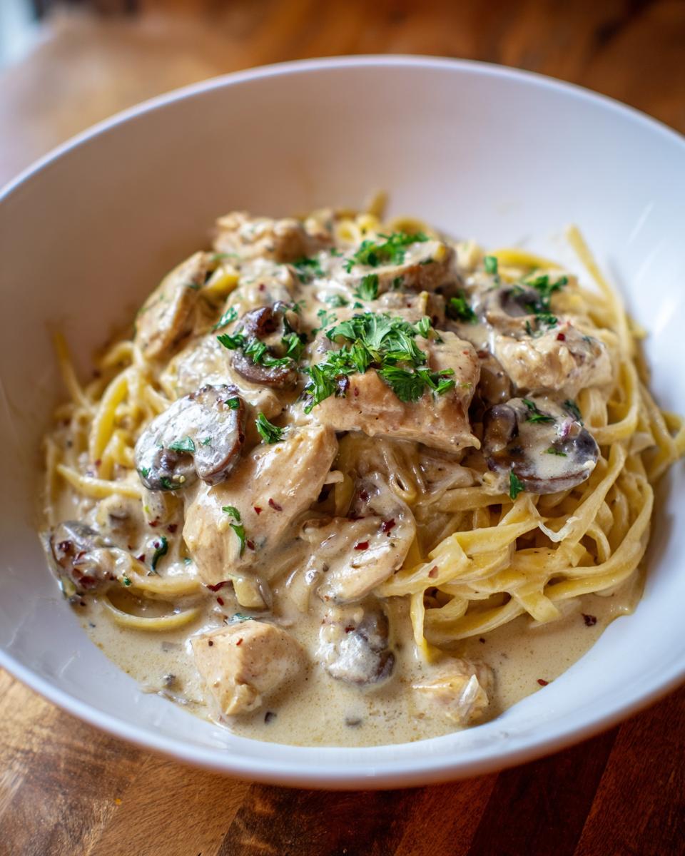 A bowl of creamy Chicken Stroganoff with mushrooms served over fettuccine pasta, garnished with fresh parsley.