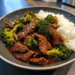 A bowl of Chinese Beef Broccoli with rice. Tender beef and broccoli in a savory sauce, topped with sesame seeds.