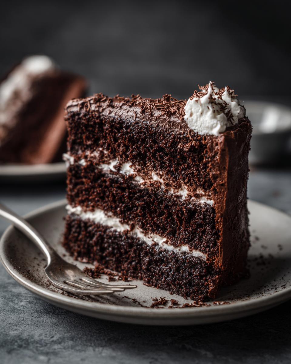 A decadent slice of The Chocolate Cake with layers of frosting, chocolate shavings, and whipped cream.