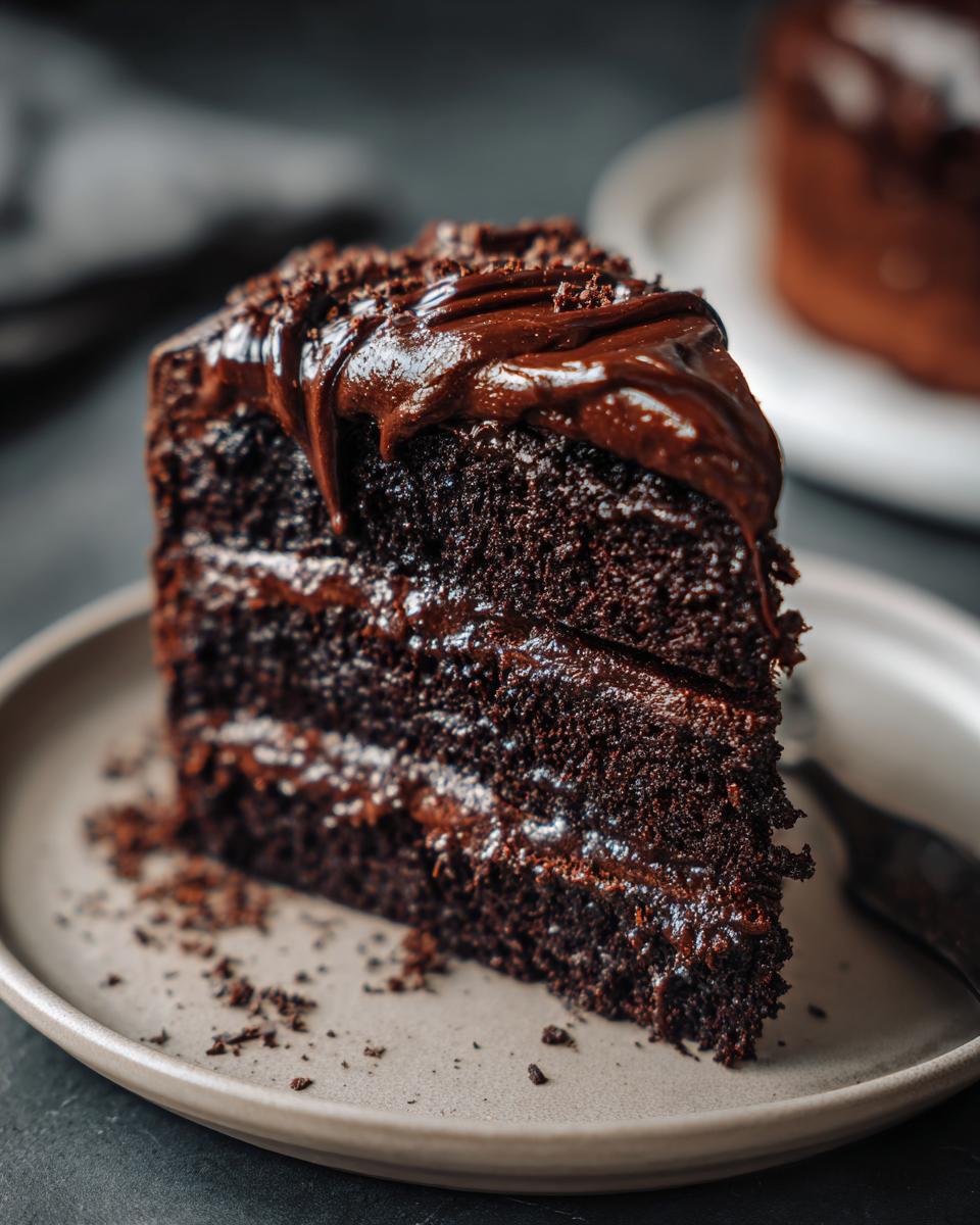 A decadent slice of The Chocolate Cake with rich fudge frosting, layered on a plate.