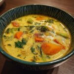 A bowl of creamy 35-Min Coconut Curry Soup with vegetables like carrots, broccoli, and spinach.