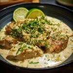Coconut Lime Chicken in a creamy sauce, garnished with lime zest and fresh herbs, served in a dark bowl.