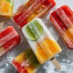 Assortment of colorful homemade Fruit Popsicles with visible fruit pieces, resting on crushed ice.