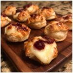 Close-up of 12-Minute Cranberry Brie Bites on a wooden board, showcasing melted brie and cranberry topping.