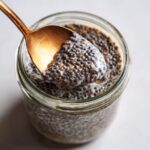 Golden spoon scoops creamy chia pudding base from a glass jar, showcasing the texture.