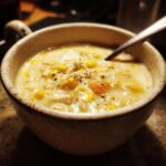 A bowl of creamy chicken corn chowder with visible corn, chicken, and seasonings. Spoon inside.
