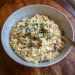 A bowl of Creamy Crockpot Chicken and Rice, garnished with parsley and parmesan cheese.