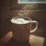 Steaming mug of Creamy White Hot Chocolate on a wooden surface, lit by window light.