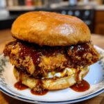 A delicious Crispy Buffalo Chicken Sandwich, topped with sauce, served on a bun.