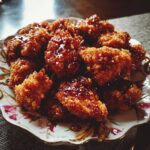 A plate of golden brown Crunchy Hot Honey Chicken pieces drizzled with a glossy honey sauce.