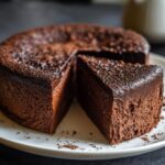 A decadent flourless chocolate torte on a white plate, with a slice cut out, showing the rich, moist texture.