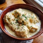 A bowl of creamy ULTIMATE Easy Chicken and Biscuits Dumplings, garnished with herbs and pepper.