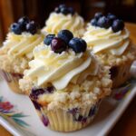 Four Fluffy Lemon Blueberry Cupcakes with white frosting and fresh blueberries on a decorative plate.