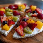 Close-up of Frozen Yogurt Bark topped with strawberries, kiwi, mango, and blueberries on a wooden board.