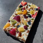 A slab of Frozen Yogurt Bark topped with strawberries, kiwi, pineapple, blueberries, nuts, and seeds.