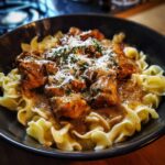 A bowl of Garlic Butter Chicken Bites Creamy Parmesan Pasta, garnished with herbs and cheese.