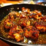 Close-up of Garlic Butter Chicken pieces in a pan, glistening with sauce and garnished with herbs.