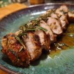Close-up of sliced Foolproof Garlic Herb Pork Tenderloin, garnished with rosemary, on a blue plate.