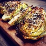 Close-up of Garlic Parmesan Melting Cabbage Wedges on a wooden board, sprinkled with herbs and cheese.