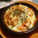 Close-up of Garlic Shrimp Gratin in a dark brown dish, topped with melted cheese and herbs.